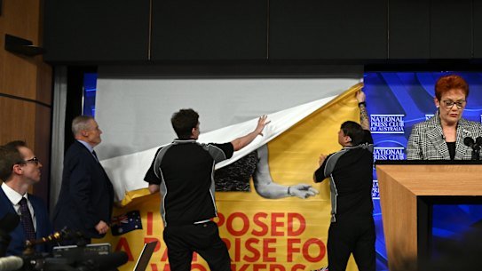 National Press Club staff remove a banner GetUp activists put up behind One Nation leader Pauline Hanson on Wednesday.