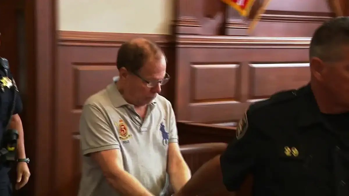 Ronald Fischer walks into a Rhode Island courtroom flanked by sheriff's deputies during his first court appearance after his arrest.