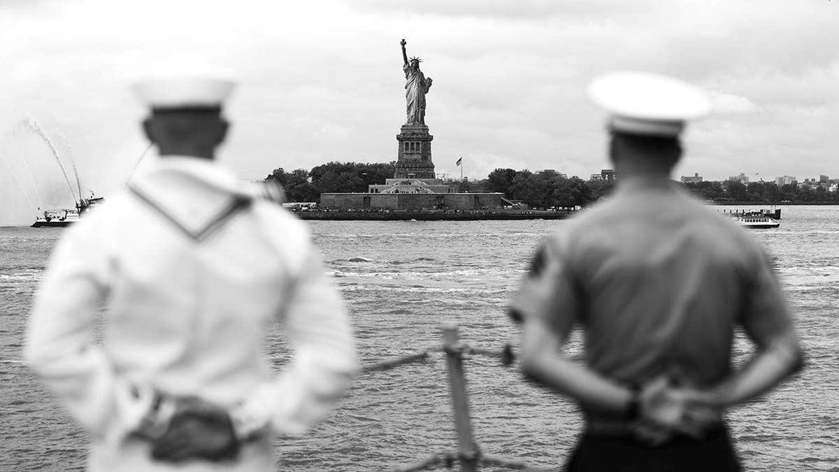 Black-and-white photograph of two U.S. service members facing the Statue of Liberty by photographer Korina Marie Moore.