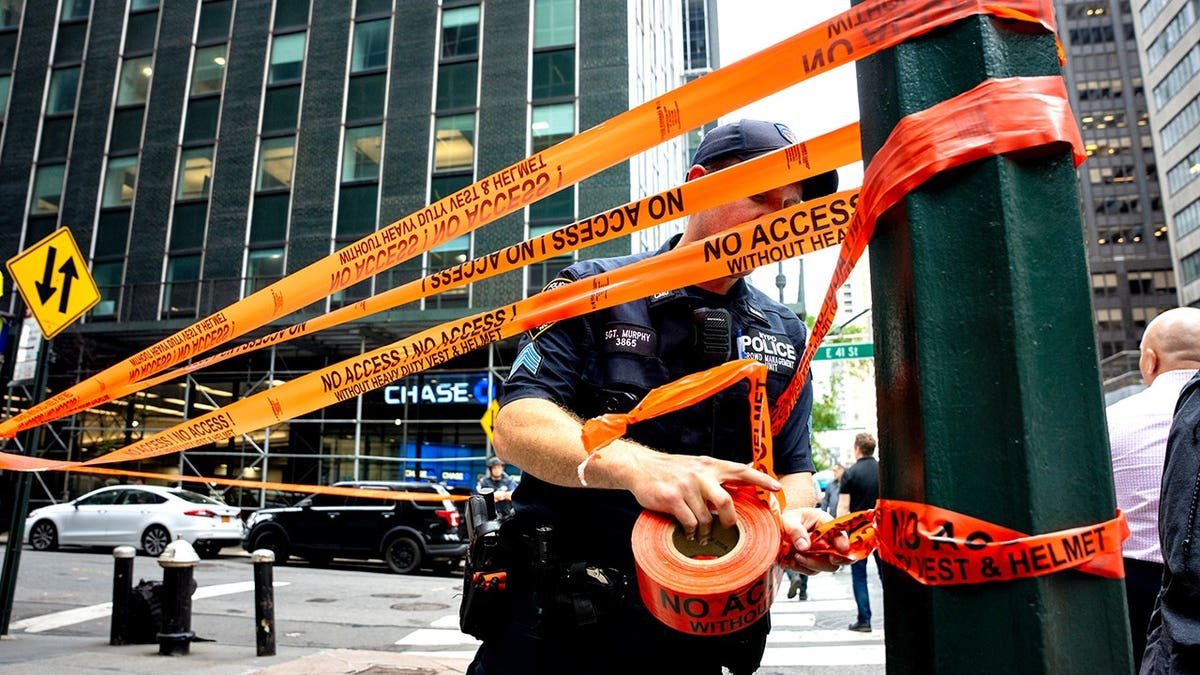 Police officer wrapping caution tape around pole and street
