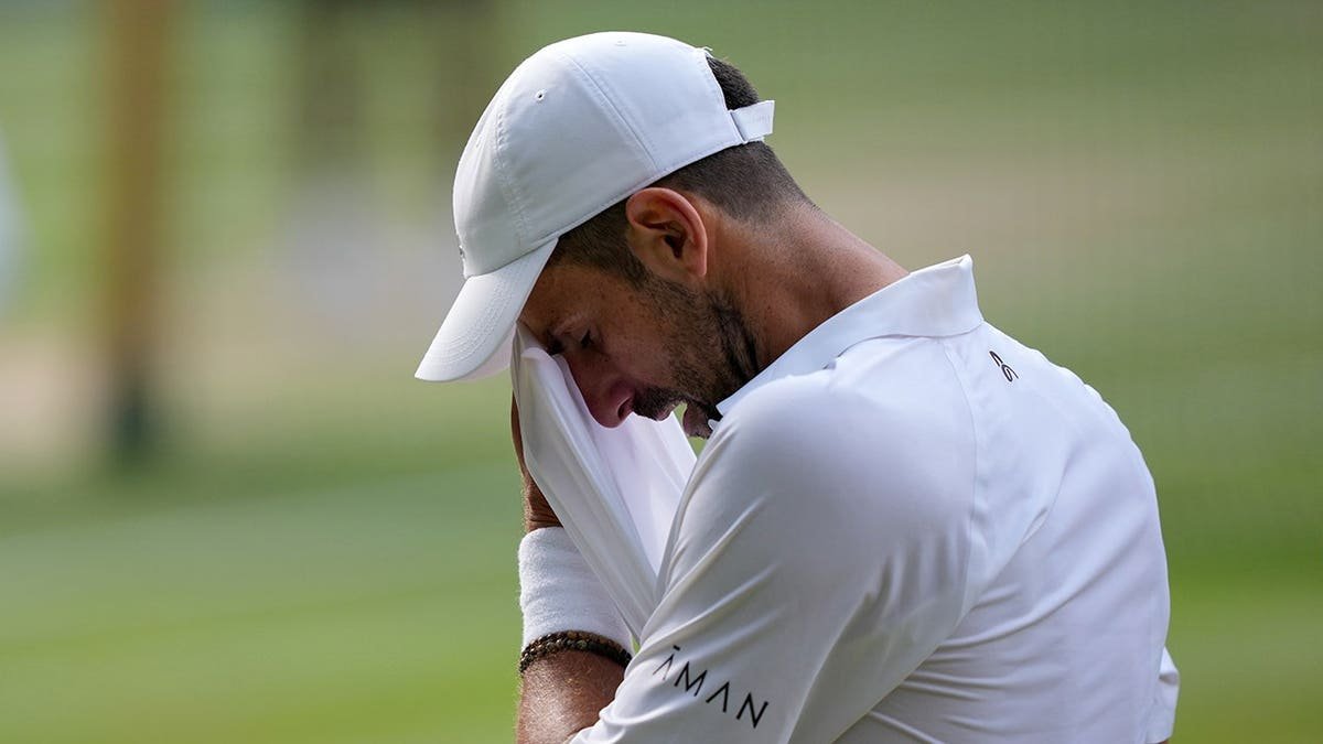 Novak Djokovic wipes away sweat during a tennis match.