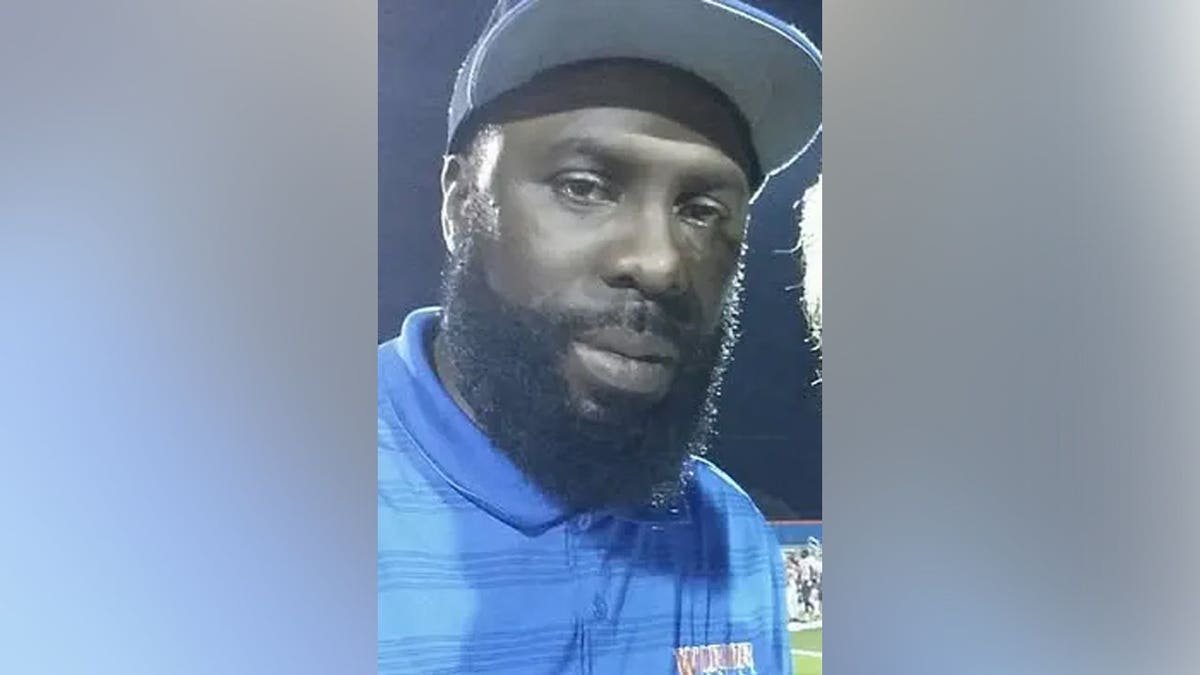 Terence Tolbert wearing a blue collared polo shirt and a gray cap, photographed on a football field at night.