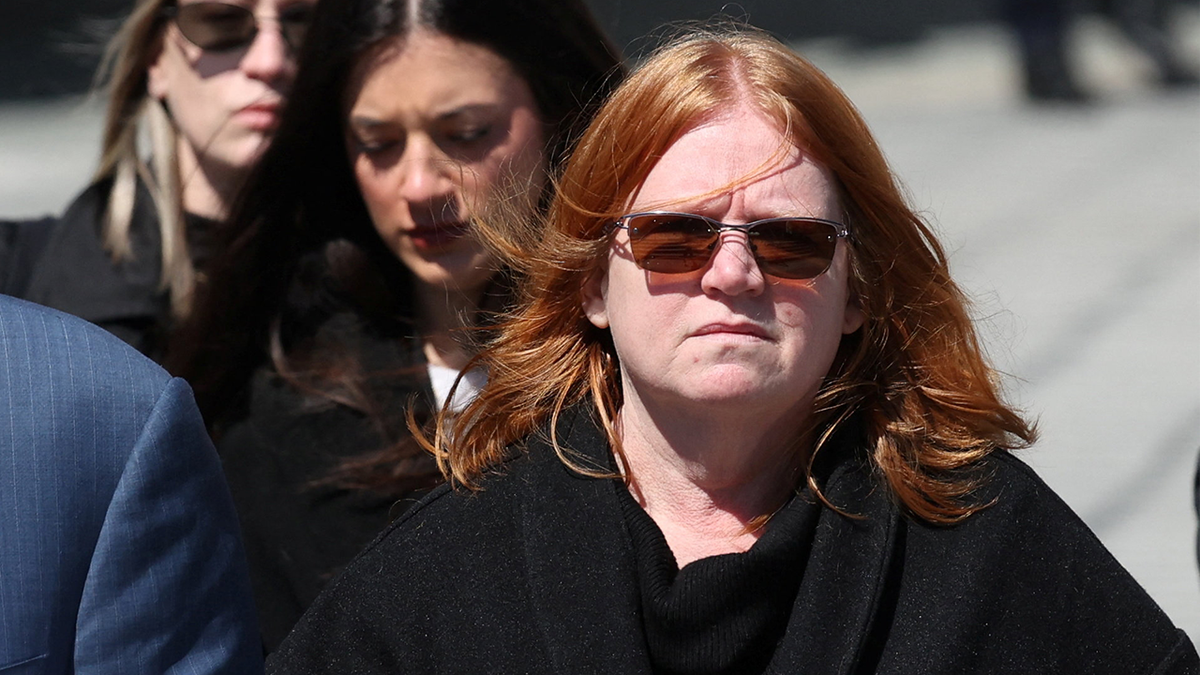 Asa Ellerup is wearing all black and sunglasses outside the Suffolk County Court in Riverhead, N.Y. She has red hair blowing in the wind.