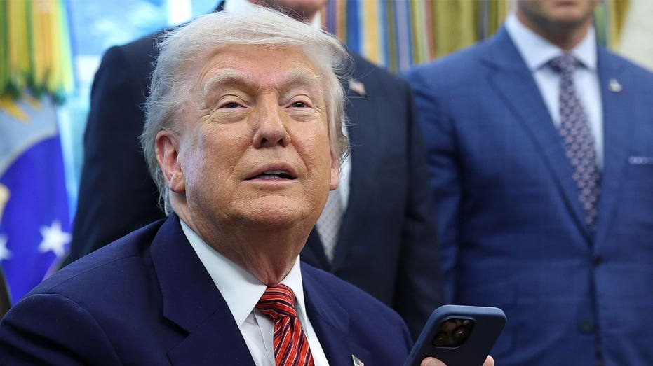 President Donald Trump holds a smartphone after signing executive orders in the Oval Office
