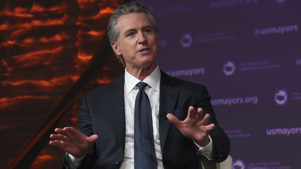 Governor Gavin Newsom standing at a podium at the United States Conference of Mayors meeting in Long Beach, California