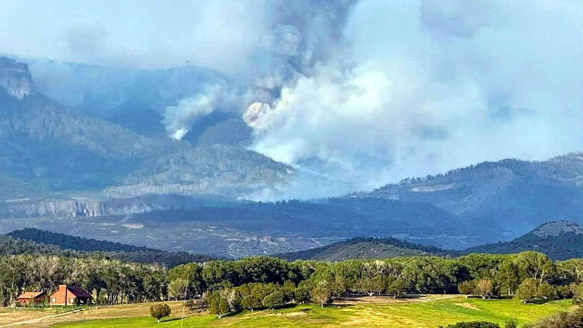 homes in foreground as smoke rises in the distance in a mountainous area