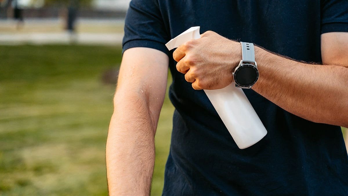 Young man applies mosquito and insect repellent spray in city park.