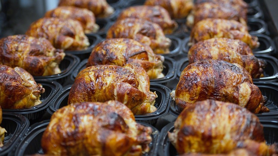 Rows of cooked rotisserie chickens in black plastic trays at a grocery store deli.
