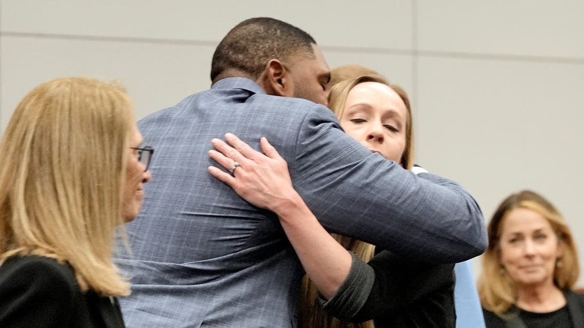 Sherrone Moore and his wife Kelli Moore hug in a courtroom after a ruling.
