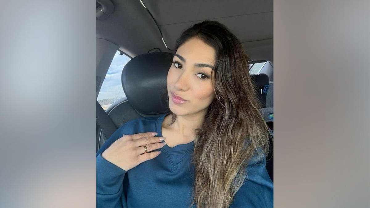 A woman in a blue sweatshirt takes a selfie in the driver's seat of a car.