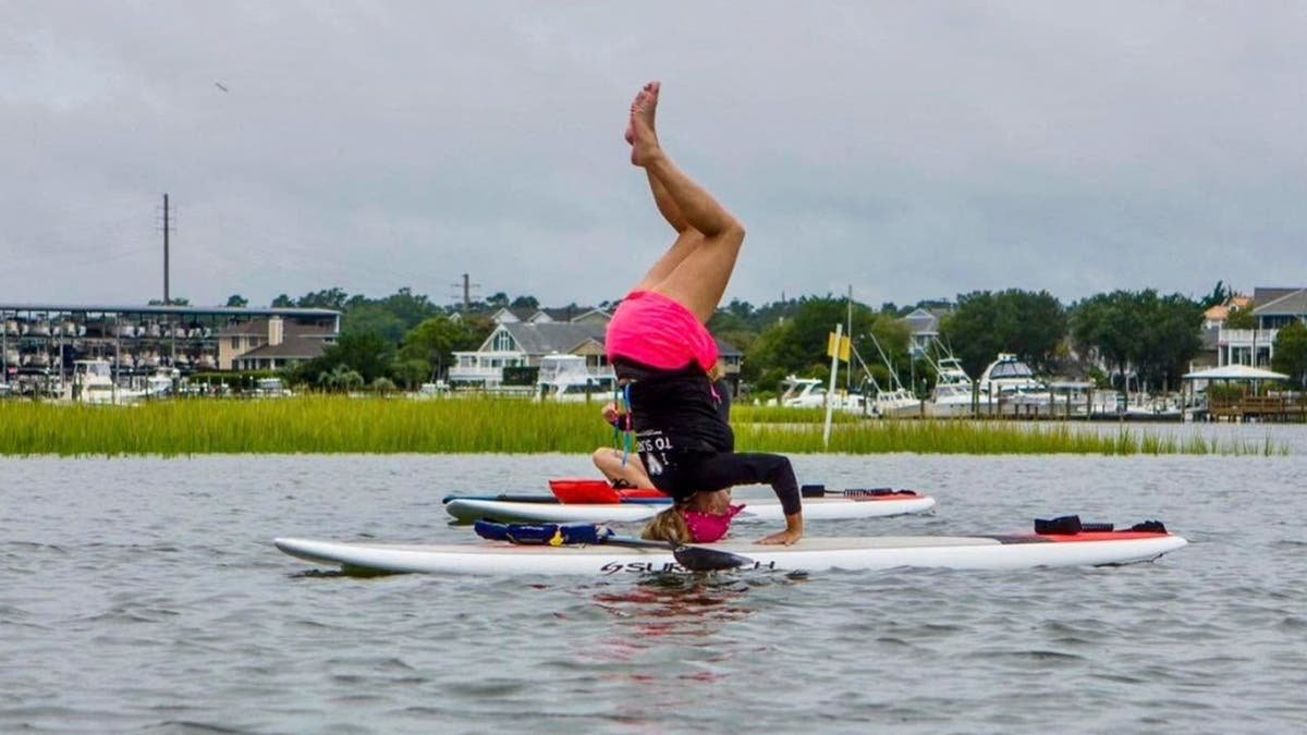 image shows Willetts standing on head while on paddleboard in water