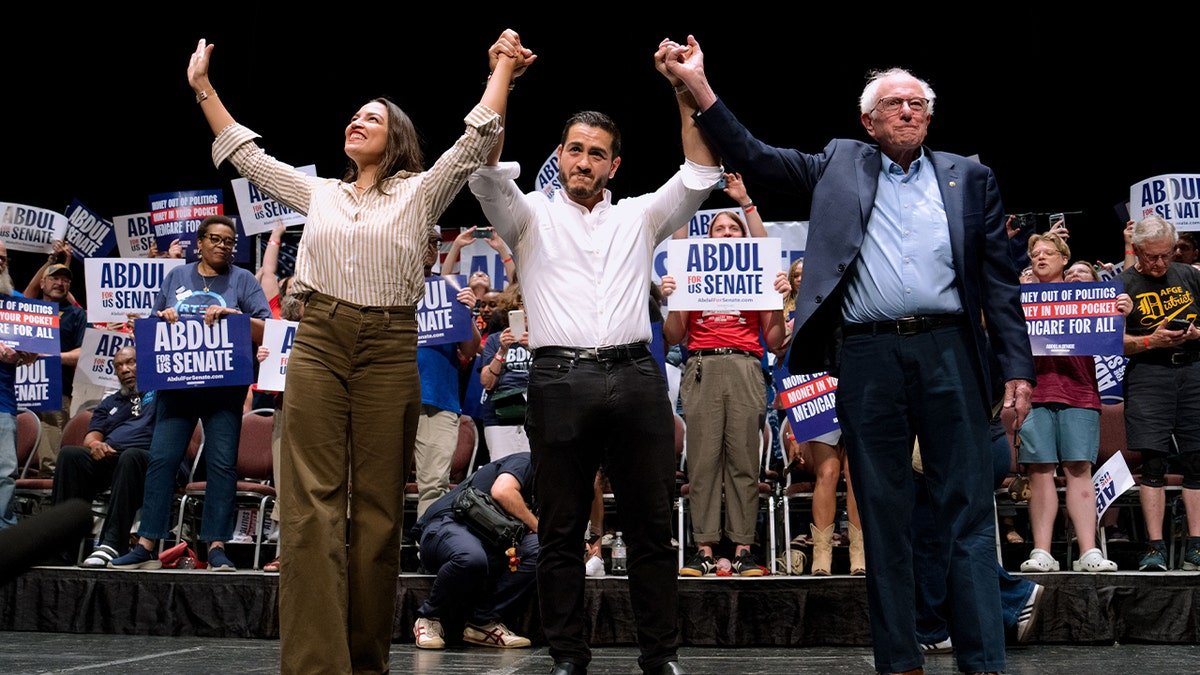 AOC, Abdul El-Sayed, and Bernie Sanders holds hands up during rally
