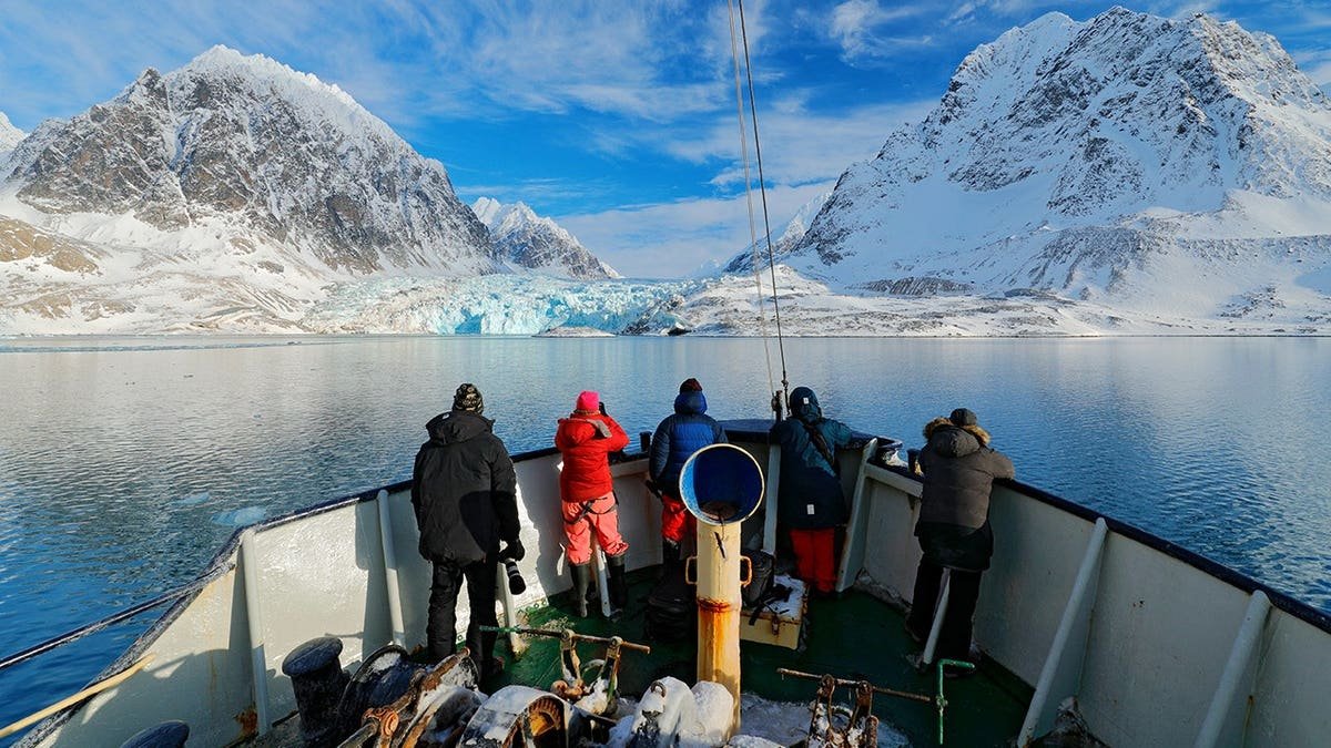 People on a boat in Arctic waters with snowy mountains and glacier ice in Svalbard, Norway.
