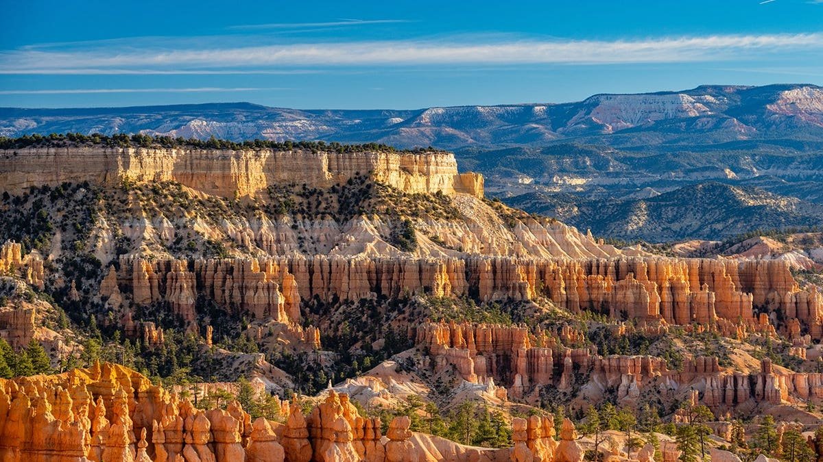 Bryce Canyon hoodoo rock formations and layered sandstone cliffs under clear blue sky at sunrise.