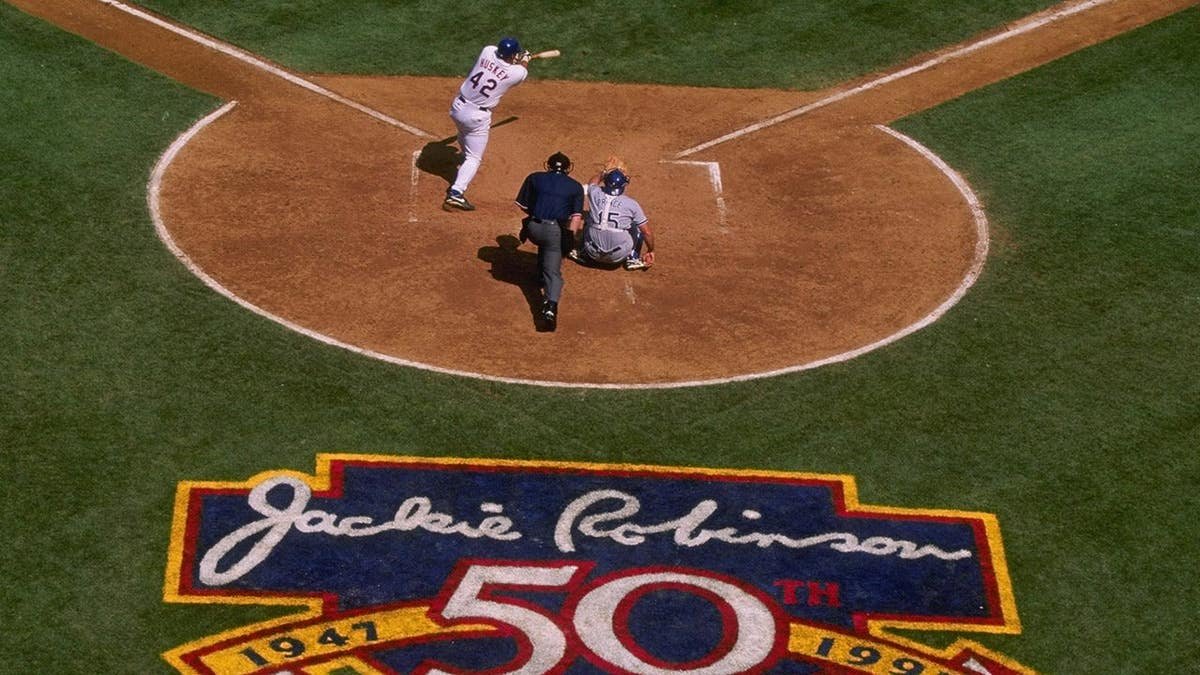 Butch Huskey of the New York Mets stands at bat behind home plate with Jackie Robinson memorial art visible on the field.