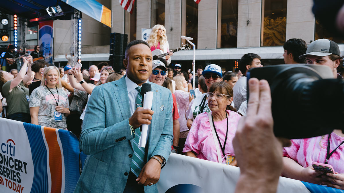 Craig Melvin in a mint green suit speaking into a microphone outside the Today studio in Manhattan