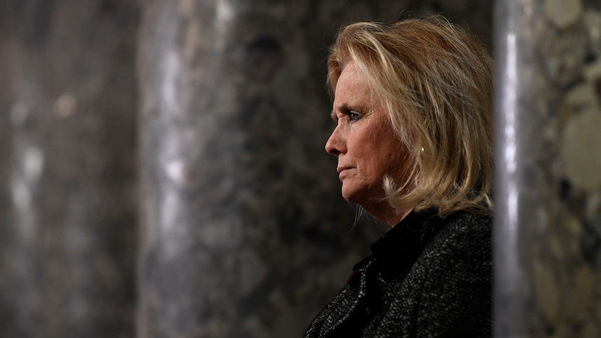 Rep. Debbie Dingell peers from beside columns