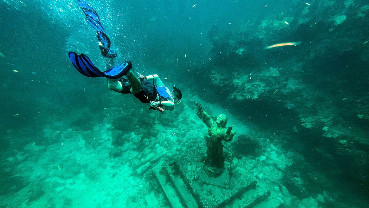 A diver swims near a submerged statue of Christ in the ocean
