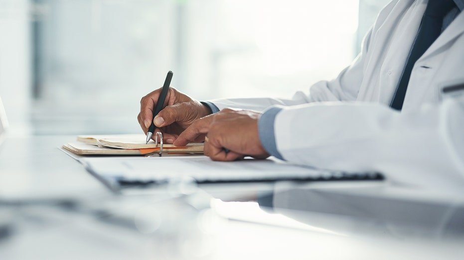 Doctor hands writing on paper or document at a desk in the hospital.