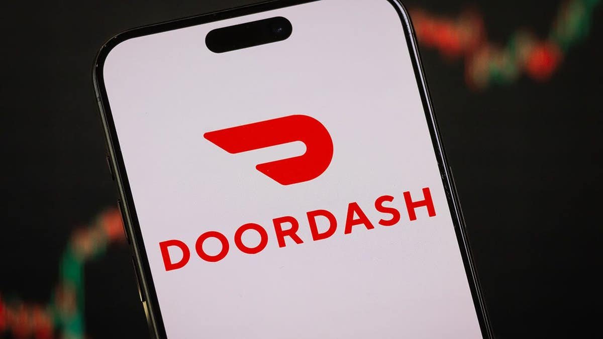 DoorDash logo appears on a smartphone screen in front of a stock chart.