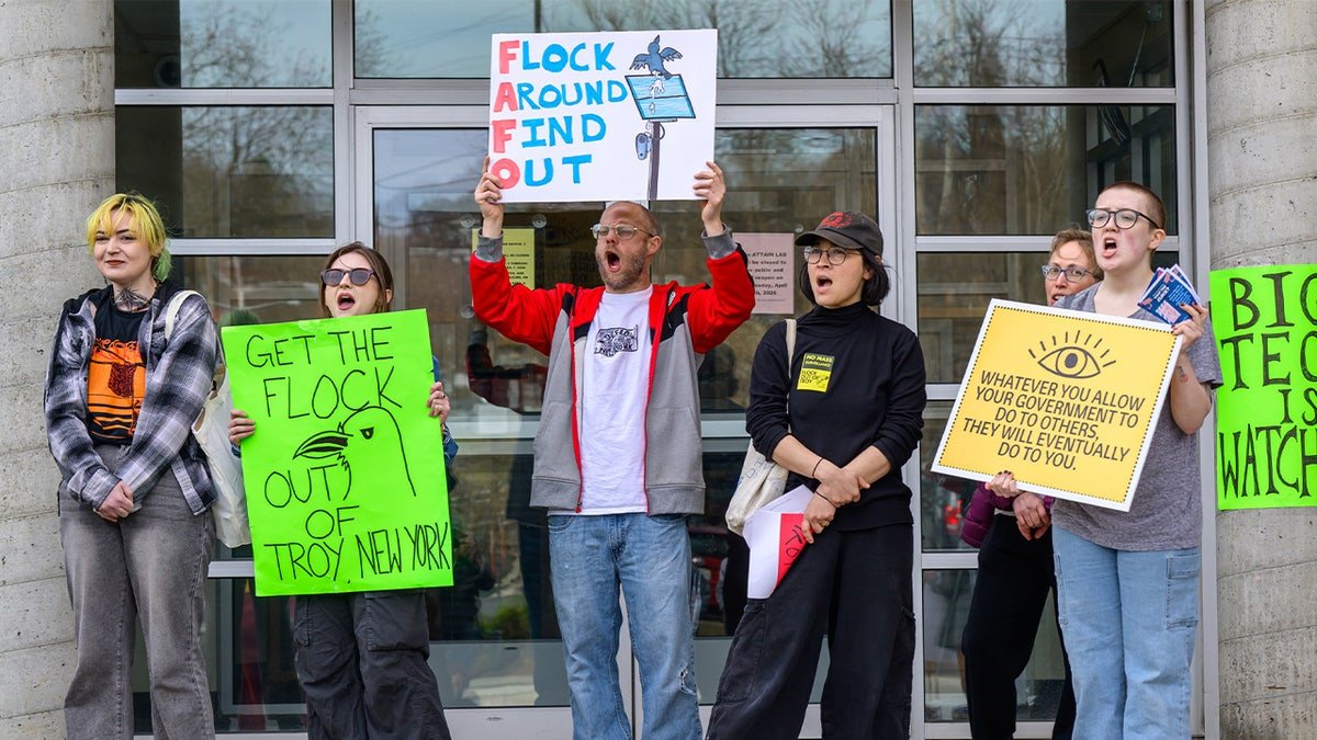 protesters hold signs demonstrating against roadside license plate cameras