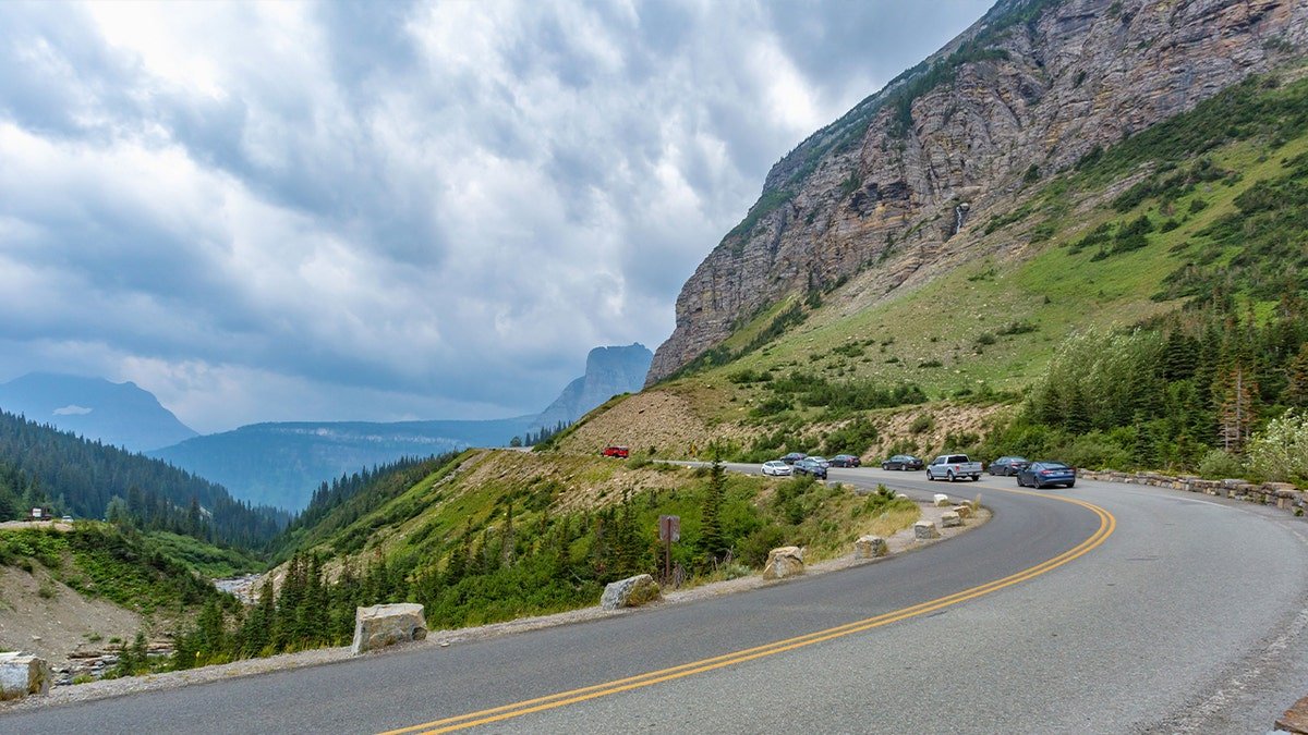 cars make a turn on a road alongside mountain
