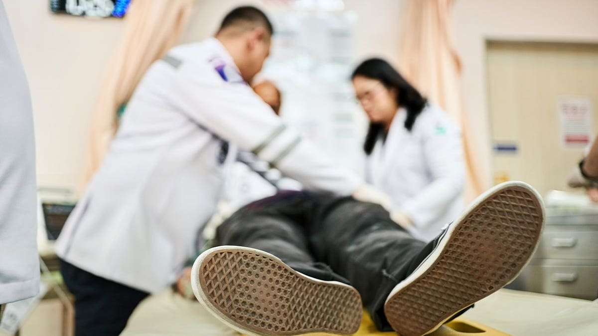 Male patient lying unconscious in a hospital bed with medical team reviving him