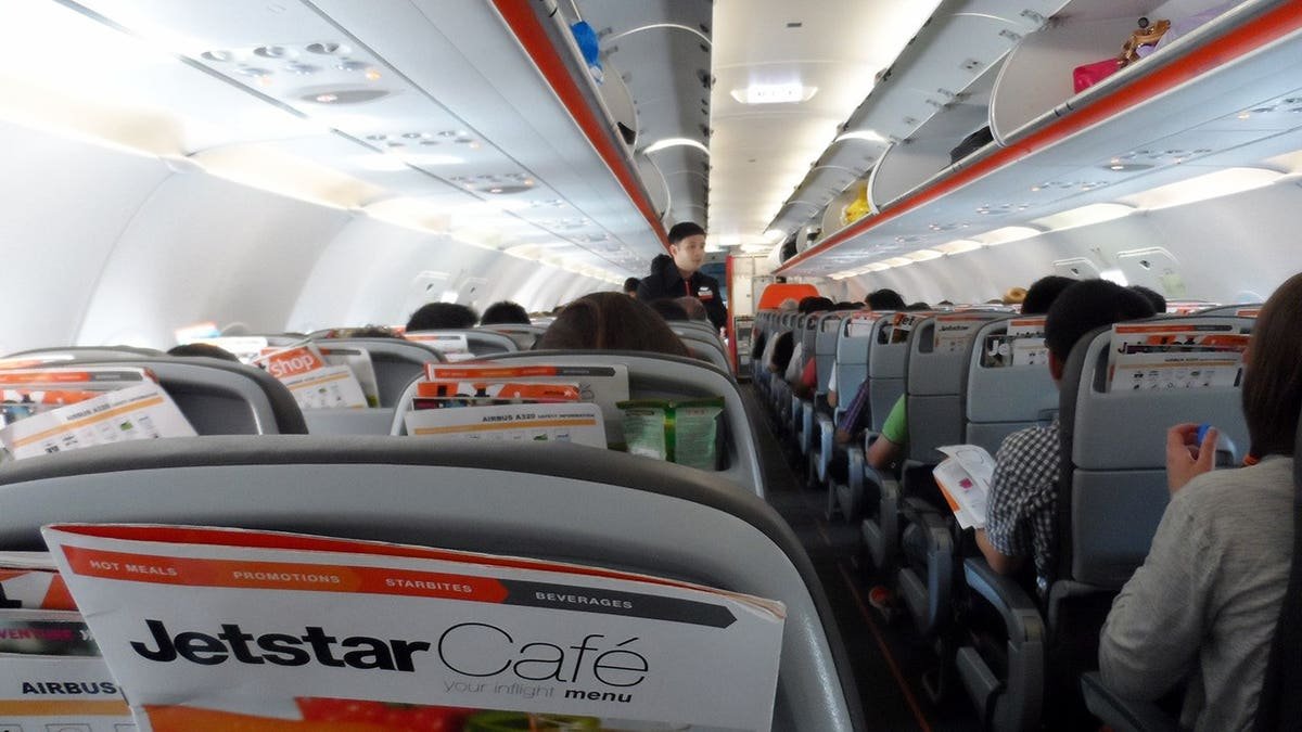 Jetstar Airways cabin interior with passenger seats, flight attendant and passengers.