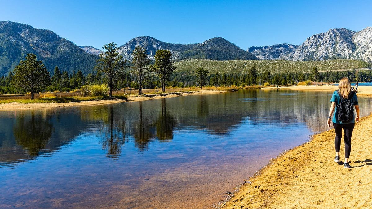 Female hiker walks on sandy shore at Kiva Beach, Lake Tahoe.