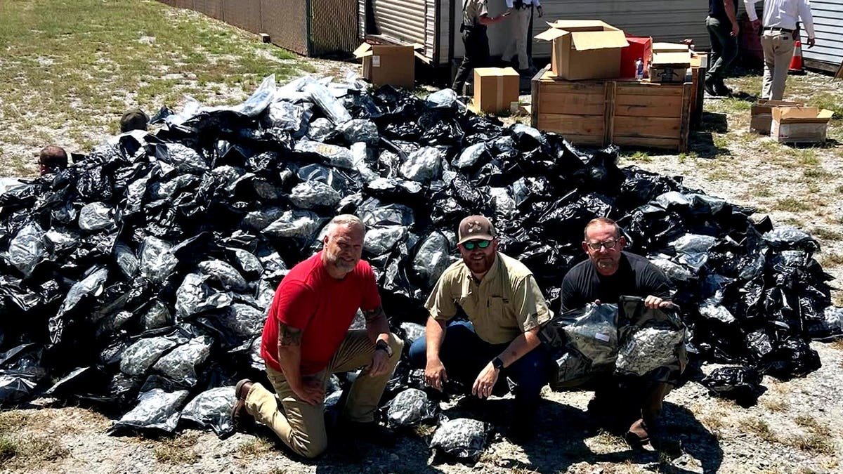 Officials standing near a mountain of suspected black market marijuana in plastic bags
