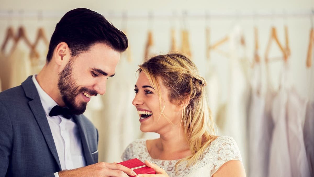 A newlywed couple laughs and holds a gift.