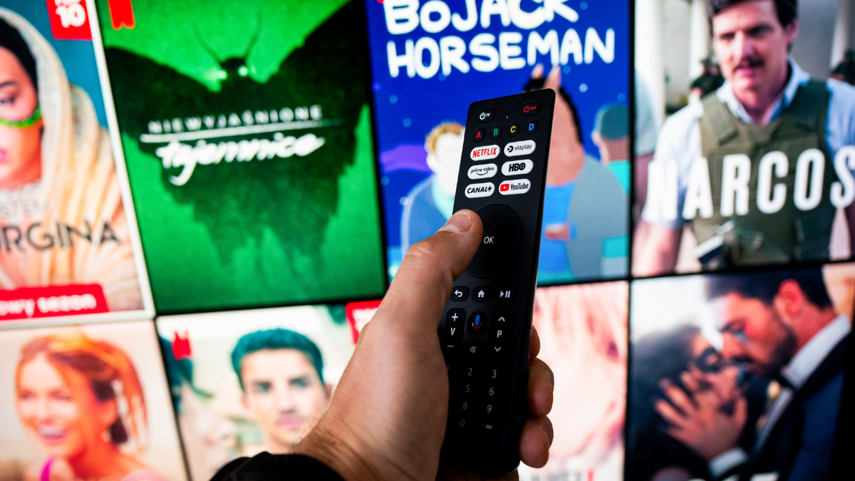In this photo illustration a Netflix logo seen on a TV remote in front of the TV.