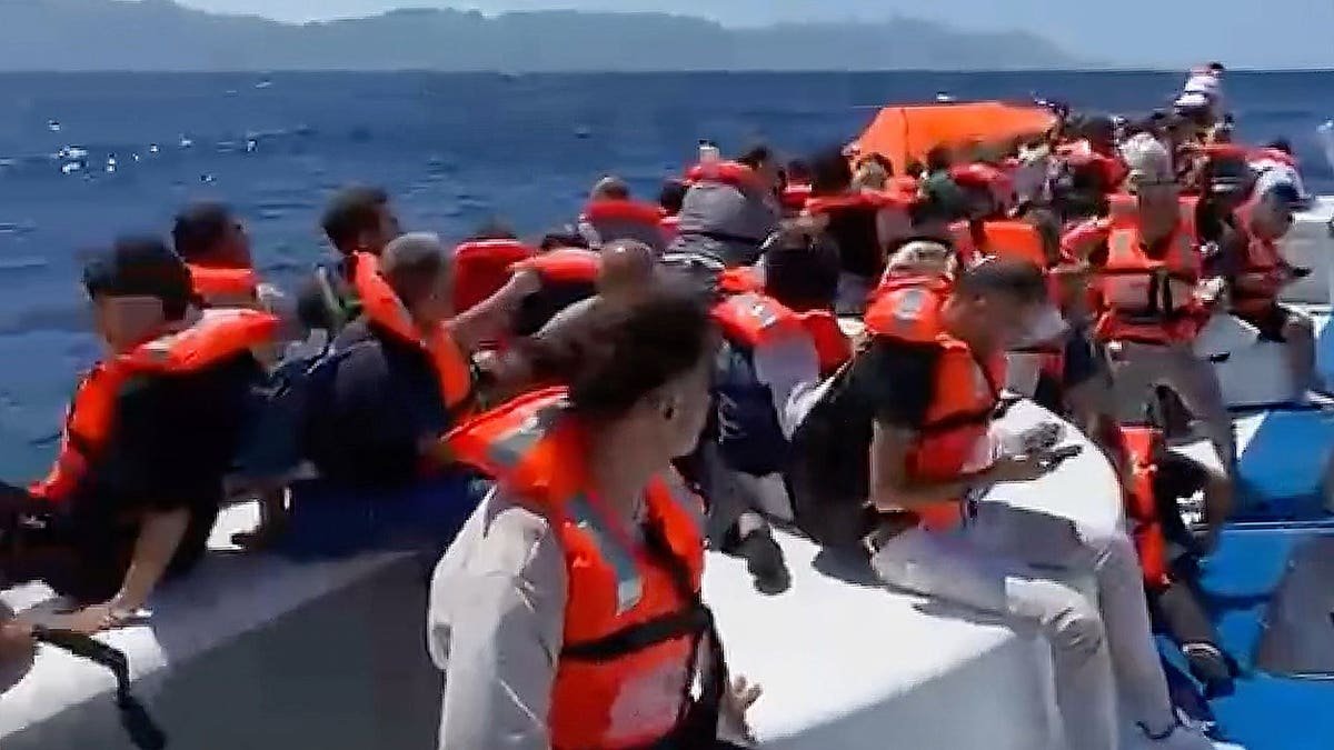 Passengers in life jackets wait atop a capsized vessel off Cyprus.