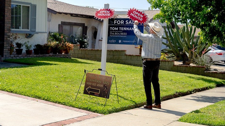 A real estate agent adjusts a sign outside a home.