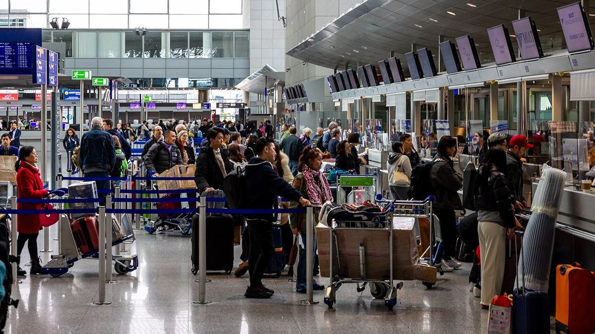 Travelers wait in line at Frankfurt Airport check-in counter with luggage carts.