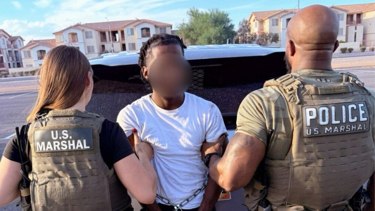 Two U.S. Marshals deputies escort Zymire Hughes, whose face is blurred, in handcuffs beside a vehicle in Las Vegas.