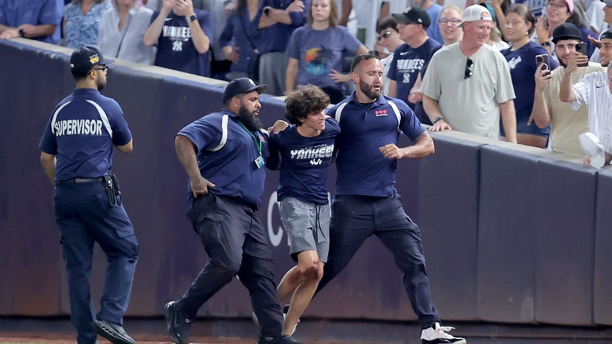 Security escorts a fan off the field during a Yankees-Mariners game at Yankee Stadium.