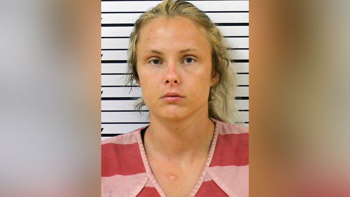 Booking photo of Geordyn Nichole Hayes, a blonde woman wearing a red-and-pink striped shirt in front of a height chart.