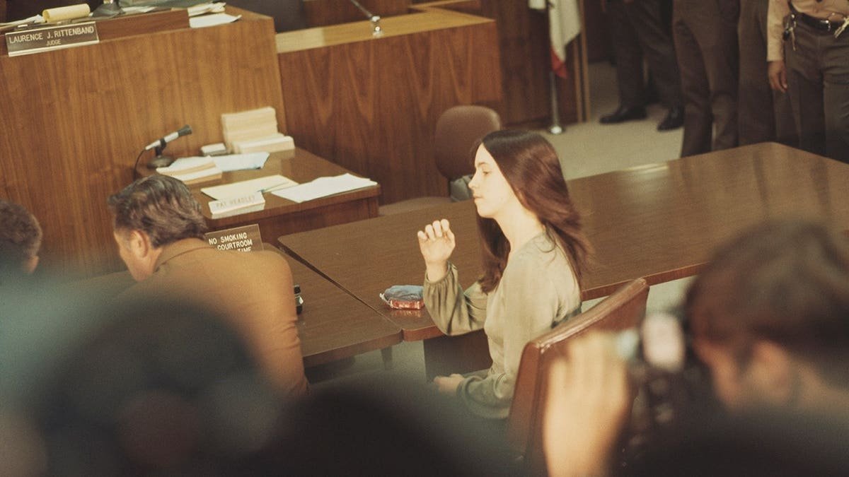Susan Atkins sits at the defendant's table in a courthouse.