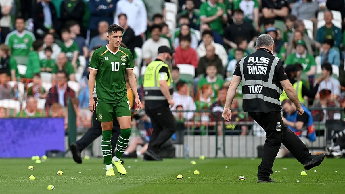 Republic of Ireland player Evan Ferguson stands on the field as tennis balls litter the pitch during a match against Qatar in Dublin.