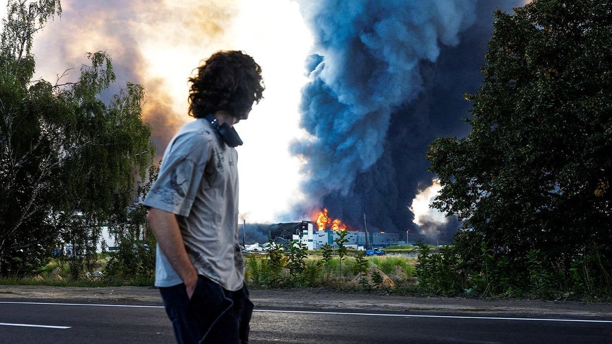 A man looks on as smoke rises over a warehouse, which was hit by a Russian drone strike, amid Russia's attack on Ukraine, in Kyiv region, Ukraine, August 27, 2026.