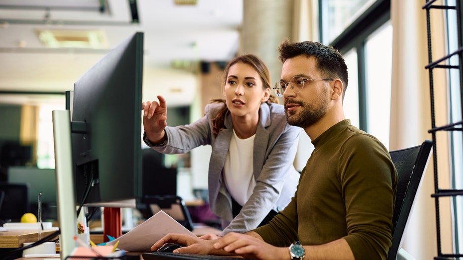 Young entrepreneur and his female coworker using desktop PC while working in the office.