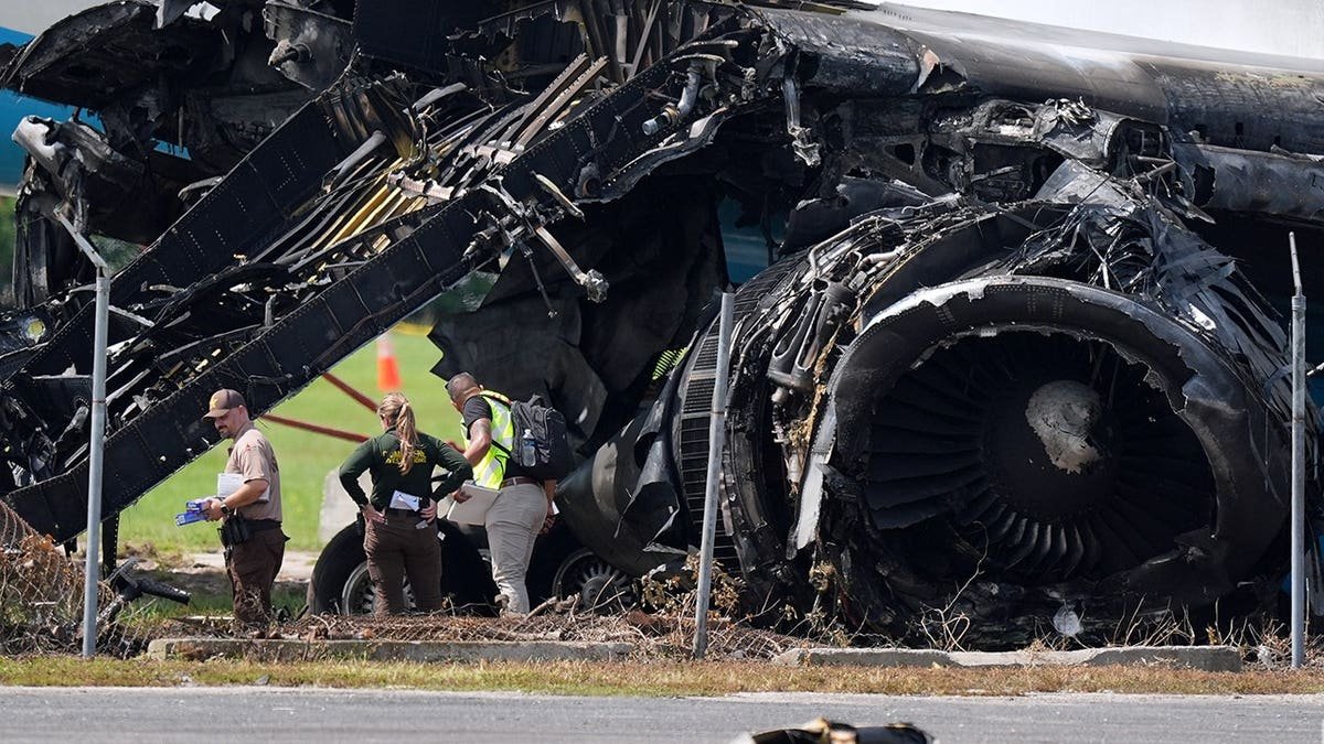 Officials stand near a destroyed wing and engine of an Amazon cargo plane.