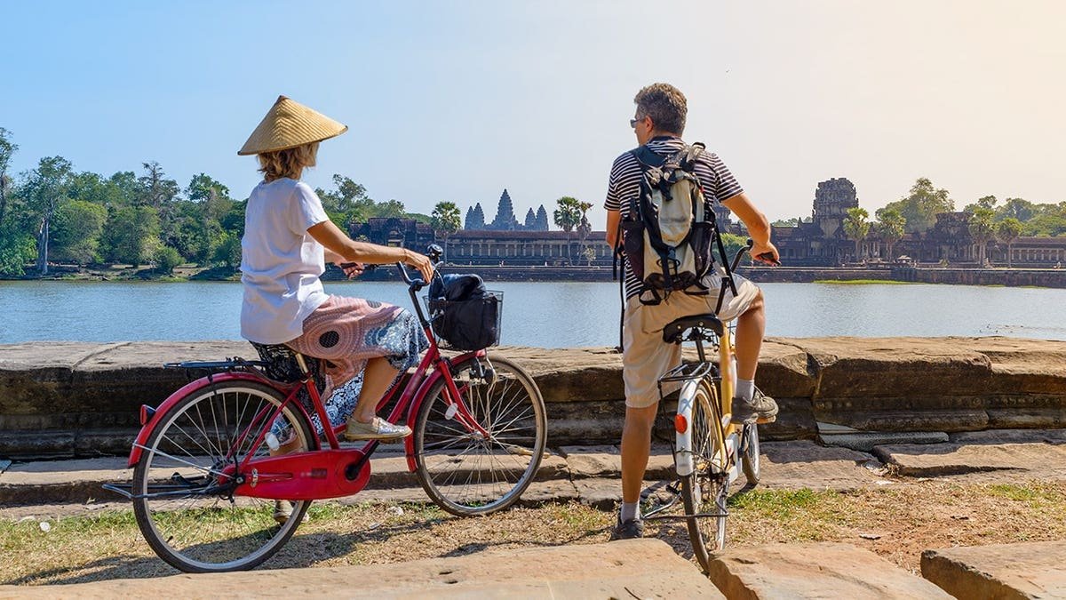 Tourist couple cycling near Angkor Wat temple in Cambodia.