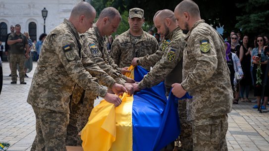 Soldiers in Kyiv fold a Ukrainian flag on the coffin of a soldier killed Russian troops in a battle.