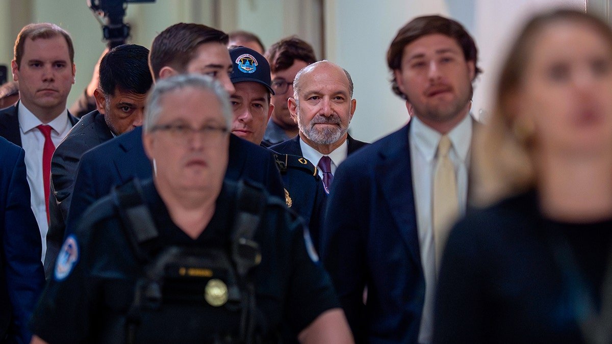 Howard Lutnick walks through a crowded hallway in the U.S. Capitol while surrounded by security and staff.