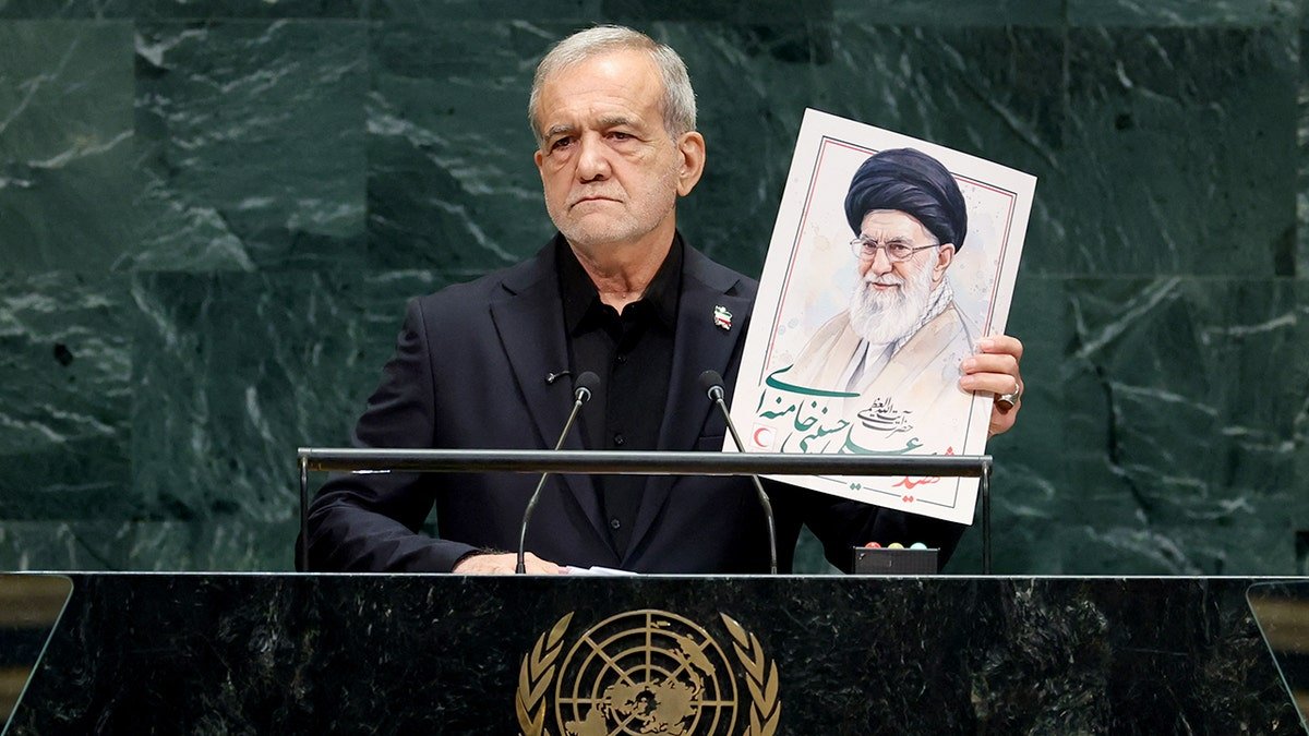 Masoud Pezeshkian holds an image of Ali Khamenei as he speaks from a podium.