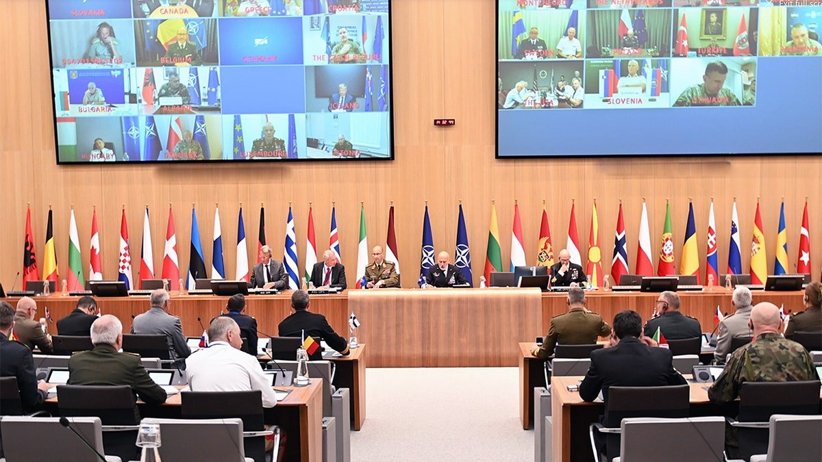 NATO defense chiefs meet in Brussels with large monitors displaying virtual participants from allied nations