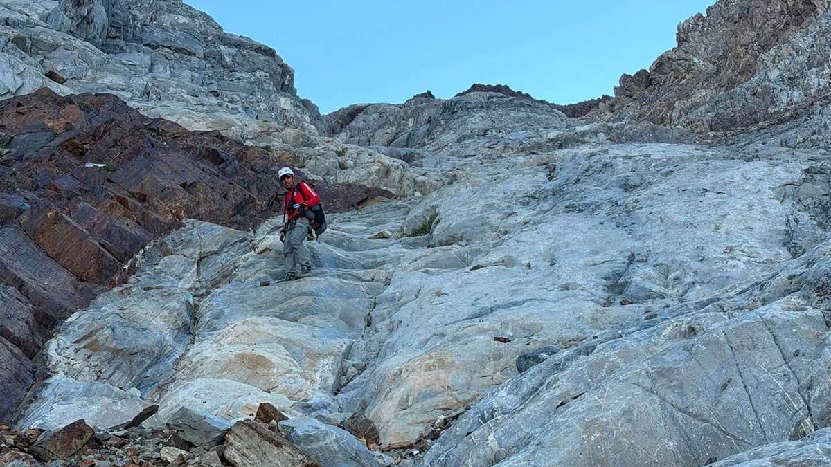 A rescuer going up the mountain to save a man stranded on a ledge.
