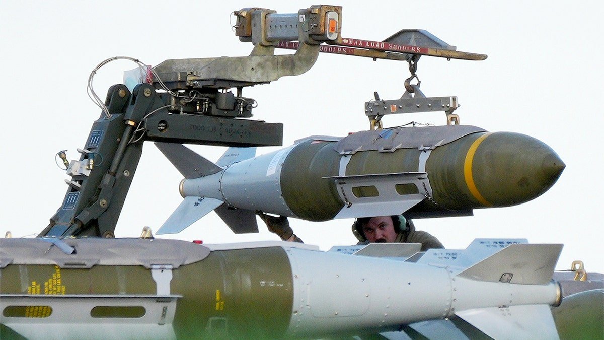Military personnel position munitions beneath a U.S. Air Force B-1 bomber on a runway at a British air base.